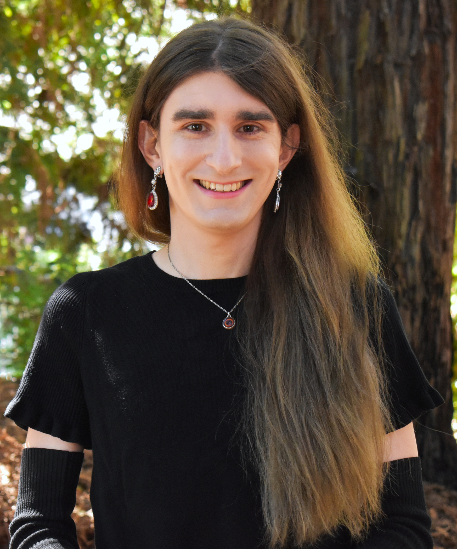 A picture of my face, taken in September 2022. I am white. I have thick, black eyebrows
	a prominant nose. I am facing the camera and smiling. I am in a well-lit, forrested area during the middle of the day. I am wearing thin-rimmed, semi-rectangular glasses.
	My hair is long, glowing with the sun at its ends, and spills across my shoulder down to my stomach. My eyes are a dark brown.